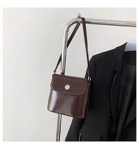 Detailopname van een glanzende chocoladebruine crossbodytas hangend bij een zwart colbert