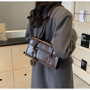 Detail view of large dark brown retro PU leather underarm bag worn by a model in gray suit