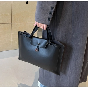 Detail of minimalist black leather tote bag featuring a flap button closure and top handles