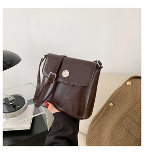 Detail van donkerbruine glanzende lederen crossbodytas met zilveren metalen gespsluiting