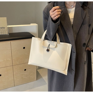 Detail of cream white leather tote bag with button drawstring closure on model's arm