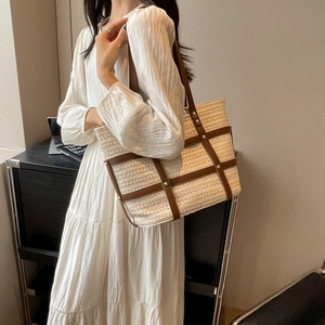 Large woven tote bag with brown leather straps shown on a model wearing a white dress