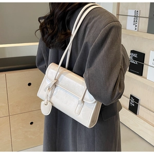 Close-up of a stylish ivory underarm bag featuring glossy leather and metallic charm