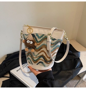 Detail of knit bucket bag featuring wave pattern, white leather trim, and plush charm