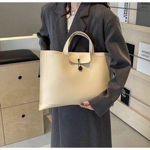 Detailed close-up of a large off-white tote bag with a front flap button design