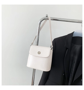 Close-up van een crème crossbodytas met zilveren m-logo detail op een zwarte blazer