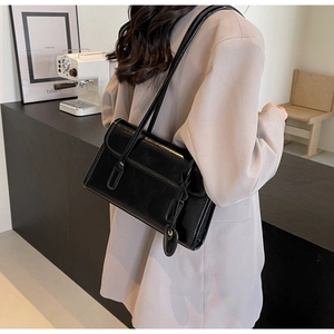Detail of minimalist black patent leather shoulder bag with a heart-shaped charm on model