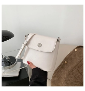 Detailopname van de crèmewitte PU-lederen crossbodytas met rond zilveren metalen logo