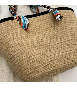 Close-up of beige woven straw handbag featuring a silk scarf handle and wooden bead accents