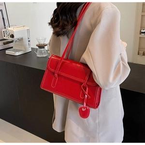 Detail of red leather shoulder bag with vintage flap and side pendant on model
