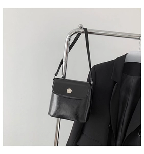 Detail van glanzende zwarte lederen tas met ronde metalen gesp en zakelijke outfit