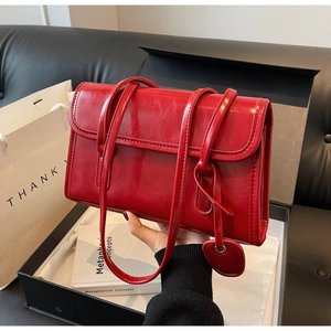Detailed shot of red oil wax leather shoulder bag with glossy finish and heart charm