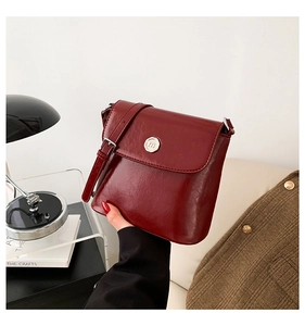 Detail van bordeauxrode crossbodytas van leer met metalen gesp en glanzende wasafwerking