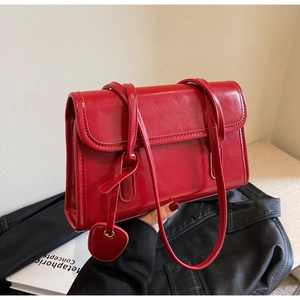 Detail of red leather shoulder bag with glossy finish and cute heart-shaped pendant charm