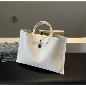 Detail of cream white tote bag with front pocket and button closure on a textured surface