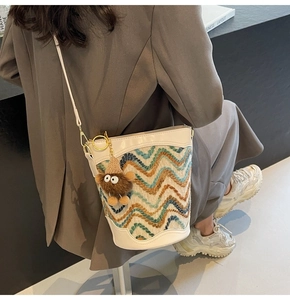 Detail of cream bucket bag with wave-knit pattern and plush charm on a model