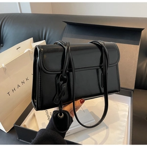 Detail of glossy black leather tote bag with heart charm and dual slim straps