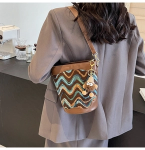 Detailed view of knitted bucket bag with brown leather strap and fuzzy monster charm