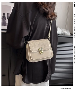 Detail of cream crossbody bag featuring embossed rabbit pattern and gold metal rabbit clasp