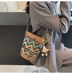Detail of woven bucket bag featuring brown leather trim and a quirky plush monster charm