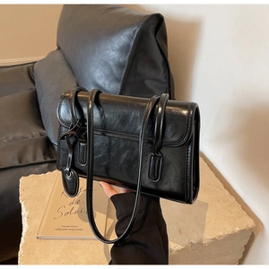 Detail of glossy black leather shoulder bag with textured pleats on stone pedestal