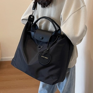 Sac cabas en nylon noir avec poignées en cuir et bandoulière porté par une femme