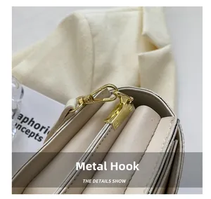 Close-up of golden metal hooks and premium beige leather stitching on a small square bag