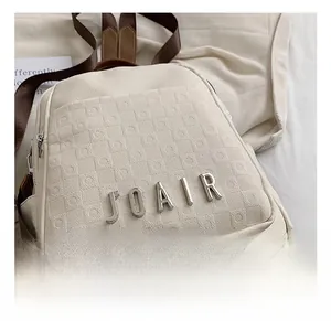 Gros plan du sac à dos en cuir gaufré beige avec logo en métal et bandoulière marron