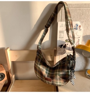 Détail du sac croissant à carreaux verts et marrons avec breloque ours sur une chaise