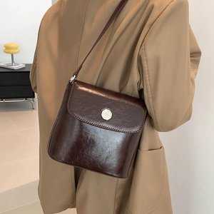 Elegante donkerbruine glanzende lederen crossbody tas met metalen gesp op een vrouwelijk model