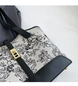 Detail of cream canvas tote bag with black floral pattern and gold twist lock closure