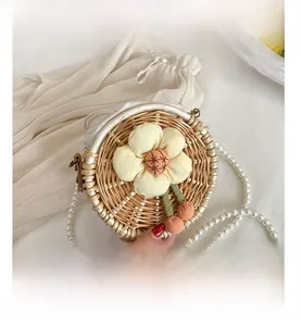 Detail of round straw woven bag with pearl strap, floral decoration and cherry pendant