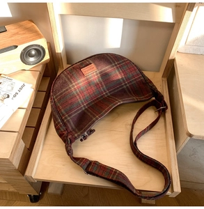 Détail du sac à main en tissu écossais rouge et vert avec écusson logo en cuir sur bureau bois