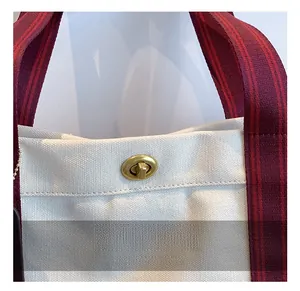 Close-up of golden metal turn-lock and striped red-black handle on a canvas tote bag