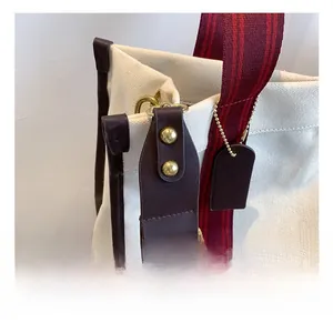 Detail of canvas tote bag showing metal hook, leather trim and striped shoulder strap