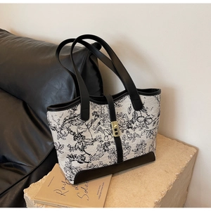 Detail of floral canvas tote bag with black leather straps and gold buckle on stone base