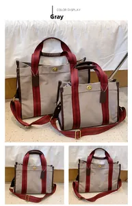 Detail view of grey canvas tote bags with red striped handles and golden turn-lock closure