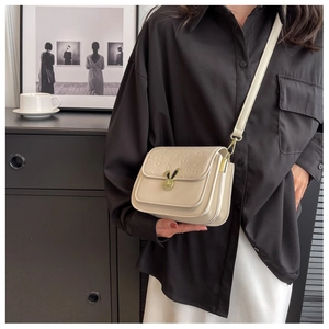 Detailed view of beige crossbody bag with bunny ear metal lock and embossed texture