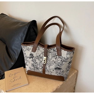 Detail of floral canvas tote bag with leather trim and gold buckle on stone surface