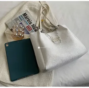Gros plan d'un sac cabas blanc à texture florale et chaîne à côté d'une tablette