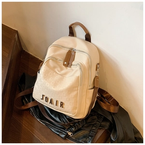 Détail d'un sac à dos crème montrant le logo en métal et la poche avant texturée
