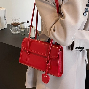 Chic red faux leather shoulder bag with heart charm shown on a beige blazer model