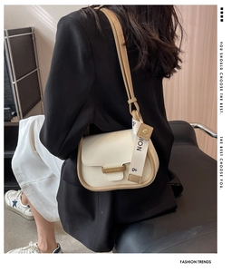 Detail of cream crossbody bag with brown piping and stylish logo strap on a model