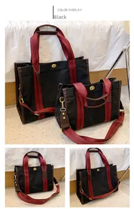 Detail view of large and small black canvas tote bags with red striped handles and metal lock