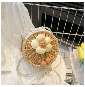 Detail of round straw woven bag with fabric flower decor and elegant pearl strap