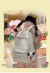 Rear view of a white PU leather backpack with a plush dog charm worn by a model in a cafe