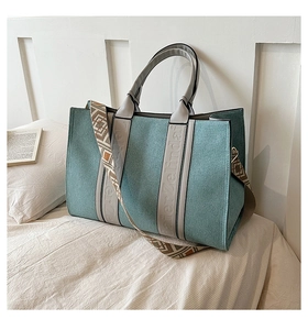 Gros plan d'un sac cabas en toile bleu canard avec poignées en cuir et bandoulière tissée