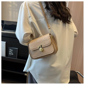 Detail of beige crossbody bag featuring embossed cartoon patterns and gold rabbit ear clasp