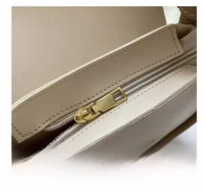 Close-up of smooth gold metal zipper and premium leather texture on the beige shoulder bag