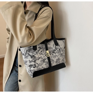 Detail of floral canvas tote bag with black leather trim and gold buckle worn by model